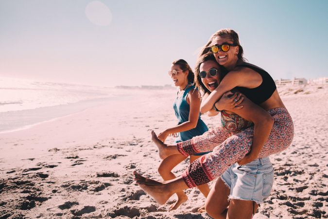 Group of smiling young women on the beach with piggyback