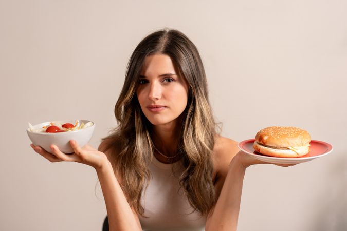 Young woman choosing between healthy salad unhealthy burger diet choice lifestyle wellness nutrition decision