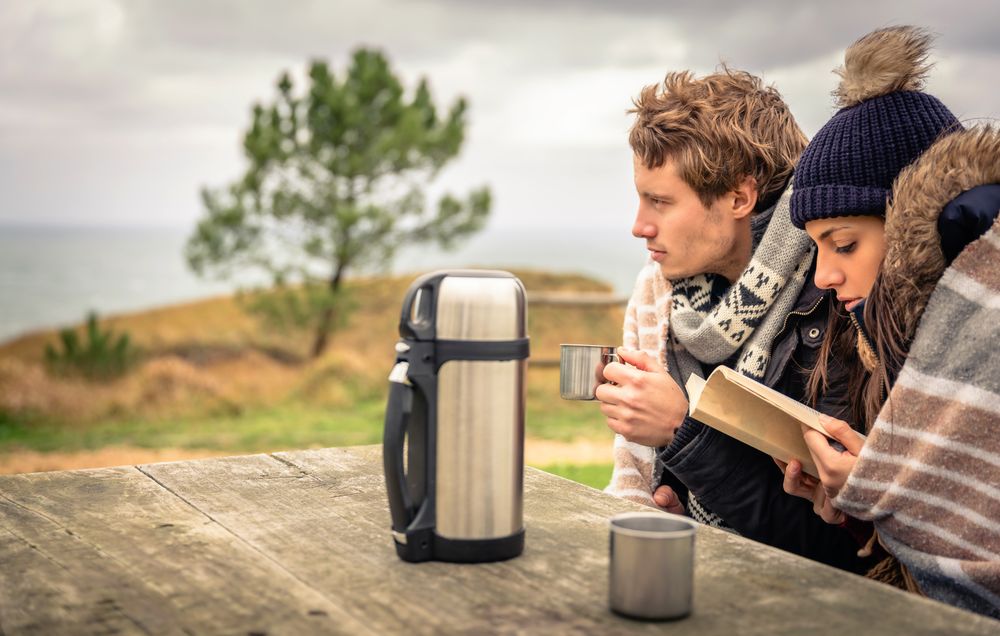 Couple sitting on park bench with flask of coffee on cold autumn day