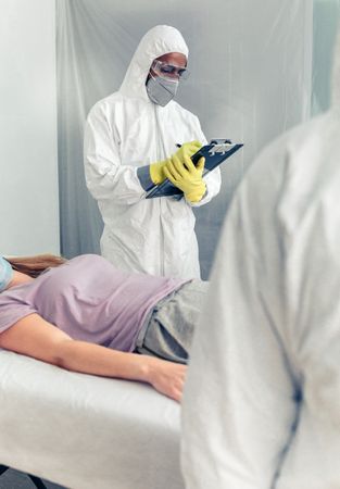 Doctors in bacteriological protection doing medical check to patient lying on a gurney