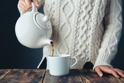 Woman pouring tea from tea pot on wooden table