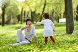 Woman with daughter playing with flowers in sunny park