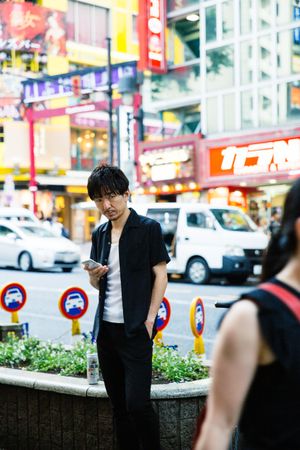 Man in dark shirt holding a phone and standing on sidewalk