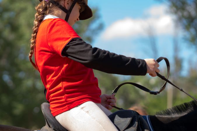 Young rider holds reins while training on horseback.