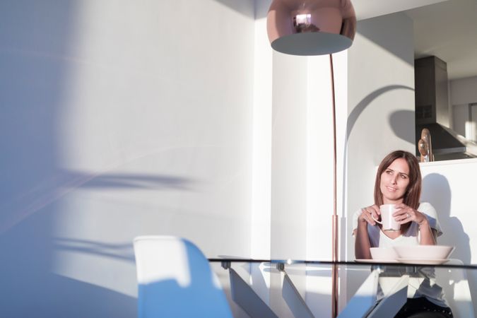 Happy woman sitting at sunny table with warm drink