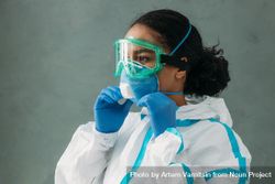 Side view of Black female medical professional in PPE gear adjusting her facemask 0JdvK4