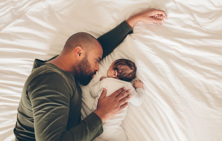 Top view of newborn baby boy sleeping with his father on bed