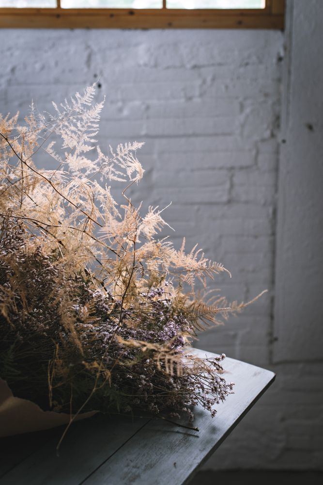 Bunch of plant in paper on table near stool in grey room