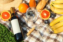 Bottle of wine, baguette, fruits, straw hat and towel on grass. Empty space