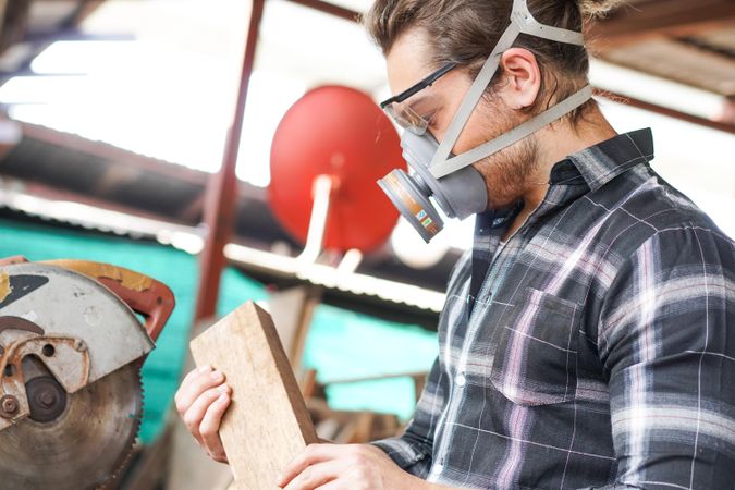 Carpenter holding wood wearing dust mask
