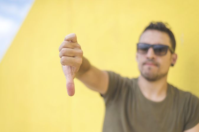 Male with thumbs down in front of yellow wall outside