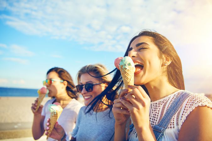 Happy female friends eating ice cream on the beach