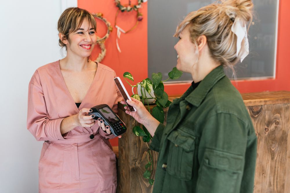 Delighted woman paying for skin care treatment with smartphone on POS terminal