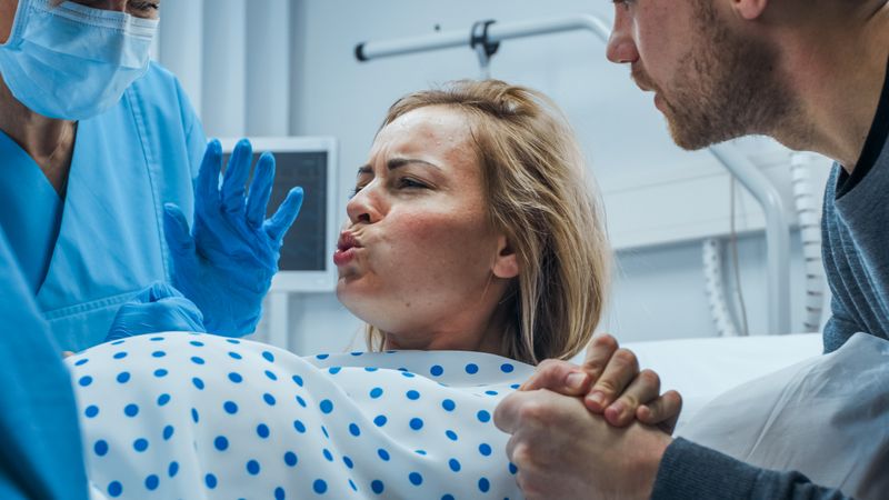 In the Hospital, Close-up on a Woman in Labor Pushing Hard to Give Birth, Obstetricians Assisting, Spouse Holds Her Hand