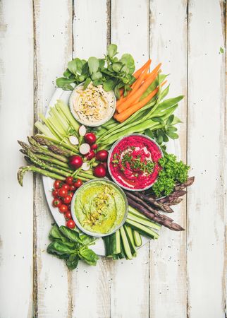 Fresh colorful vegetables and dips with hummus, avocados, asparagus, carrots on plate on table