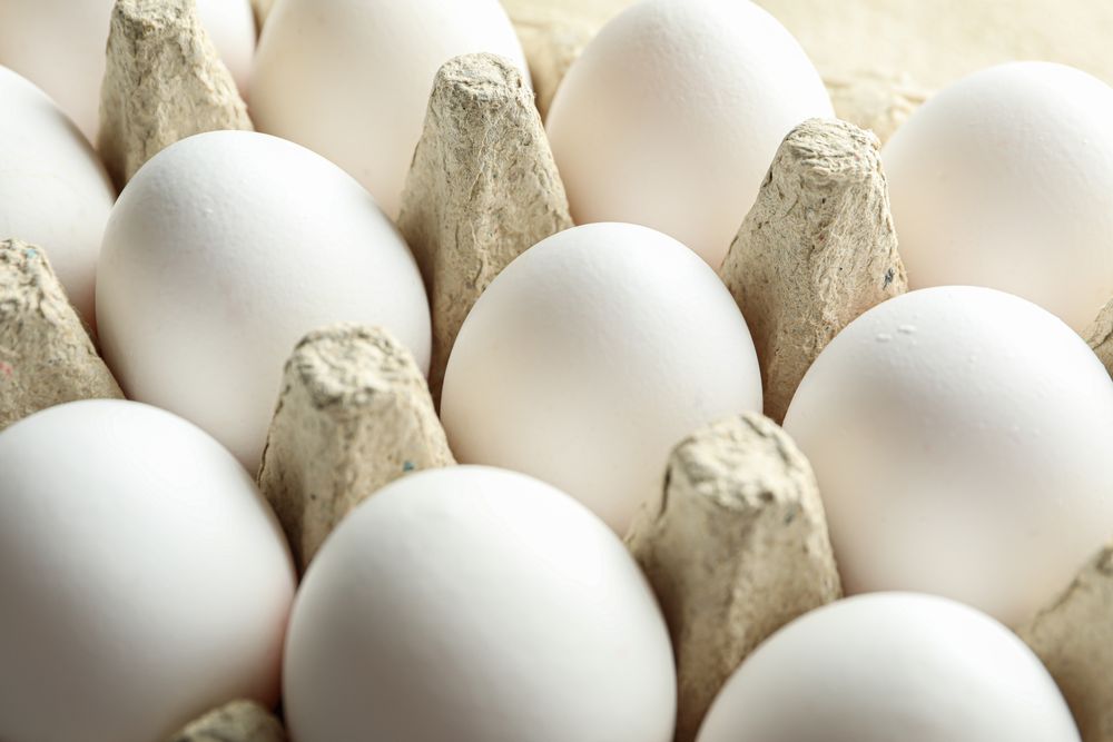 chicken eggs in carton box on wooden table, closeup
