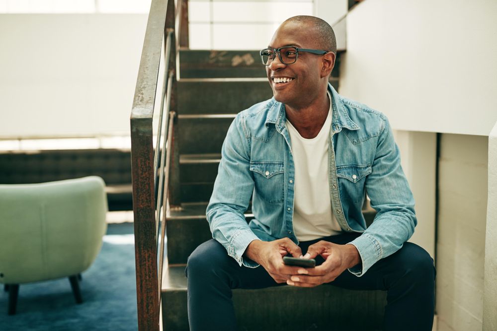 Portrait of smiling man in jean jacket on stairwell with cellphone