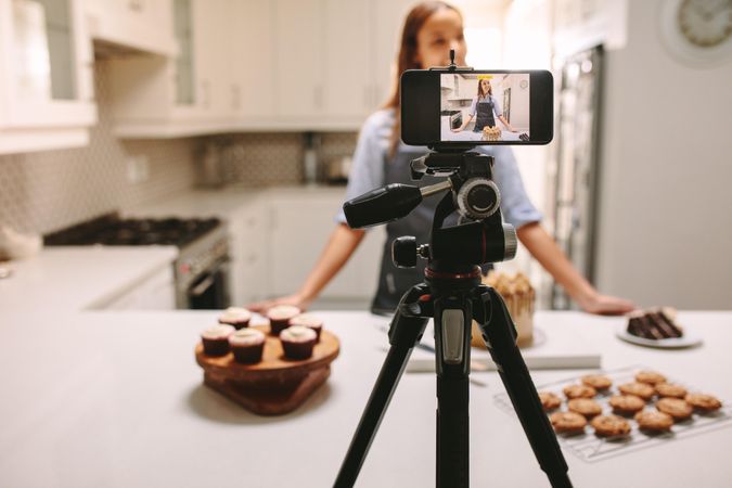 Young female blogger recording video on mobile phone camera in kitchen