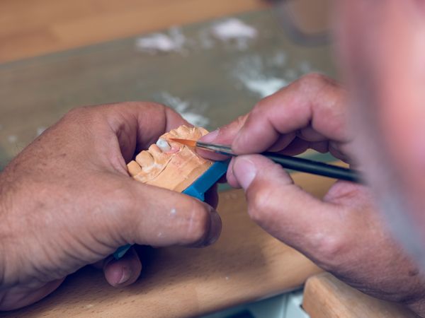 Crop man dental technician applying ceramic on denture