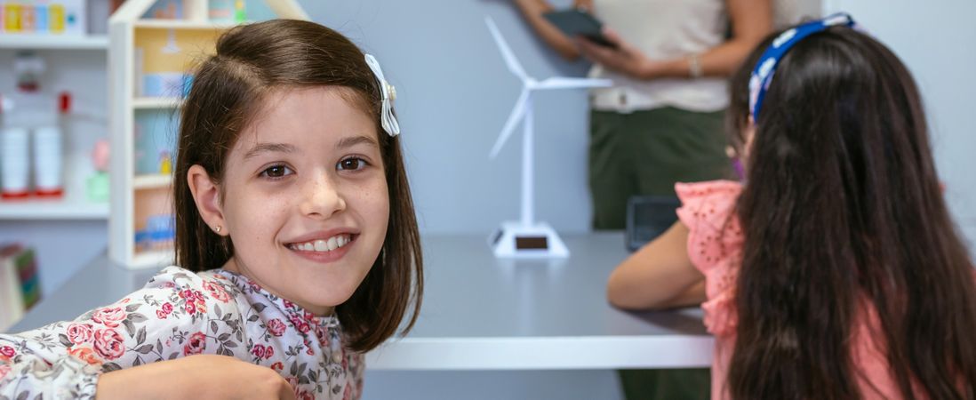 Portrait of schoolgirl in ecology classroom and teacher explaining lesson on background