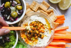 Person dipping carrot stick into hummus decorated with vegetables