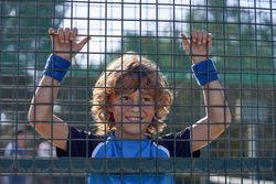 Cheerful boy hanging on metal fence on court on sunny day