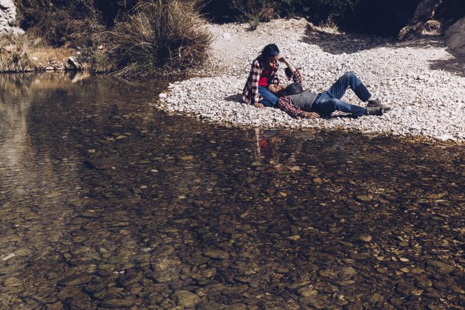 Positive woman and man resting on stone shore near river