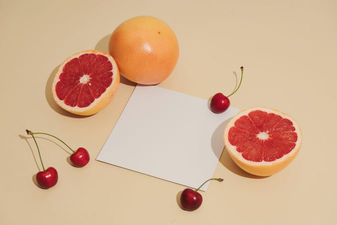 Grapefruit halved, and cherries with paper card on beige background