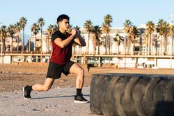 Asian sporty man doing lunges near tire