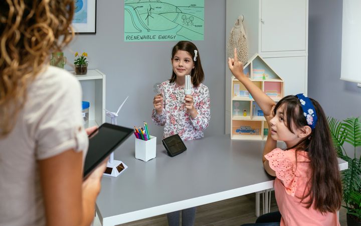 Student showing incandescent light bulb and led lamp and while her classmate raising hand