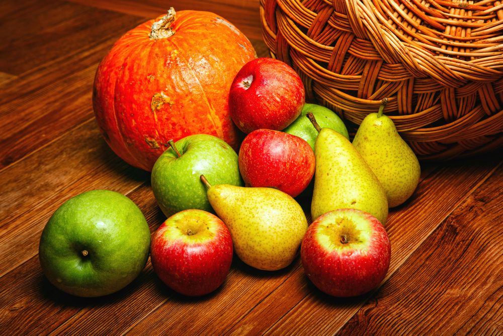 Autumnal fruit and squash on wooden table with wicker basket