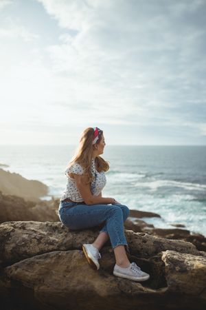 Pensive woman sitting on stone and looking at seascape