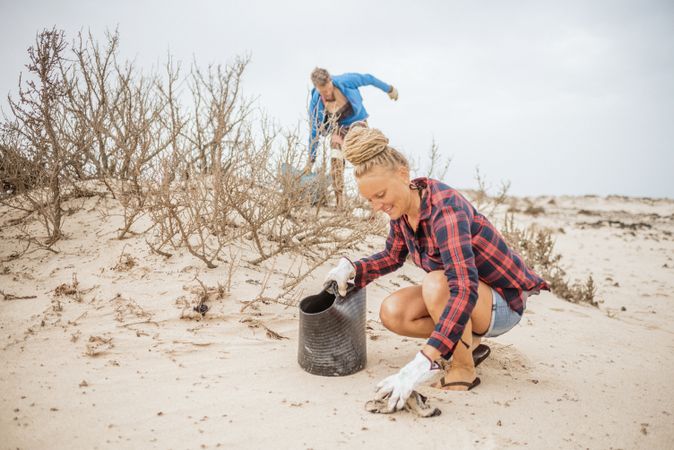 Content modern woman and man picking litter from sandy seashore