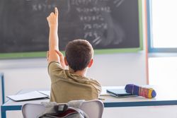 Back of teenager with one arm up to ask question in class
