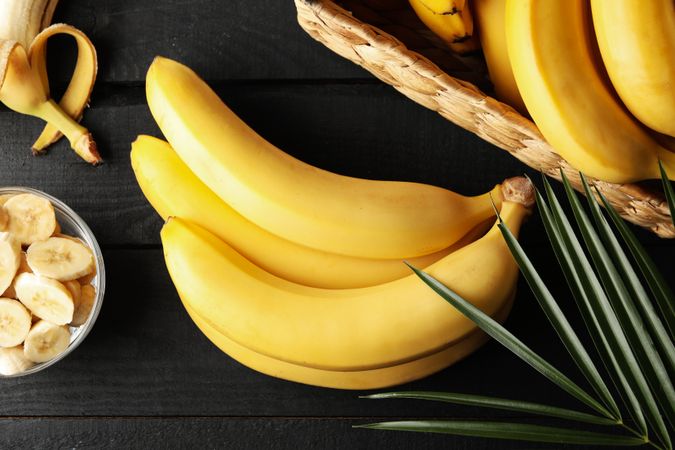 Bananas. Basket with bananas and bowl with slices on wooden background
