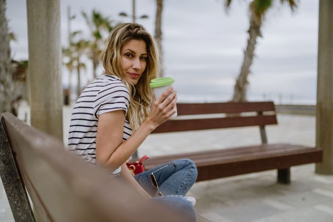 Happy woman with disposable cup of coffee sitting on street bench