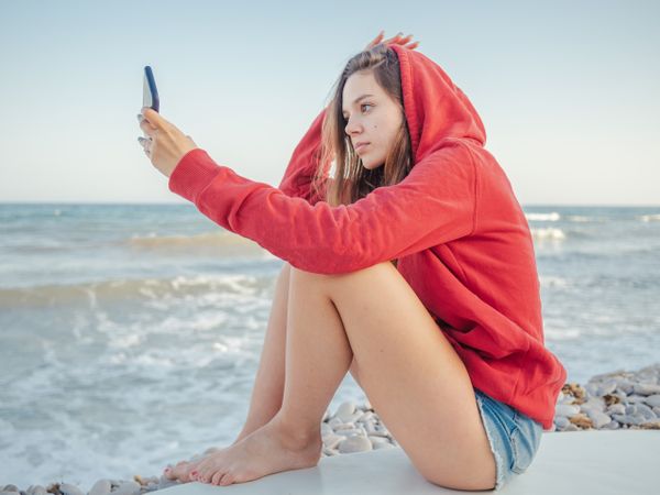 Smiling woman taking selfie lying on surfboard
