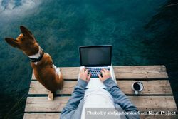 Man sitting on pier with coffee, dog and laptop 5qOKKb