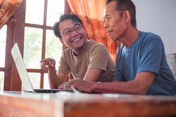 Happy adult son teaching mature father using laptop