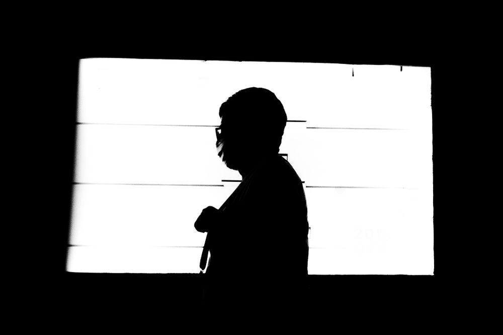 Silhouette of person in glasses and facemask walking in sunny patch of light