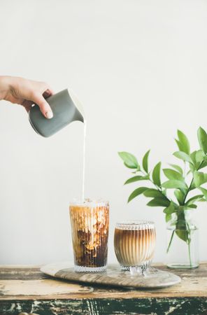 Hand pouring cream into iced coffee, vertical composition