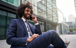 Joyful man in suit sitting outside and talking phone