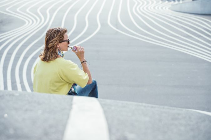 Modern relaxed woman vaping while sitting on marked road