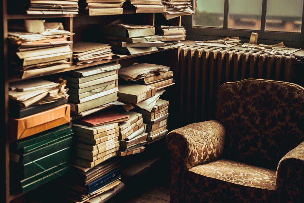 Old armchair near shelves with heap of papers