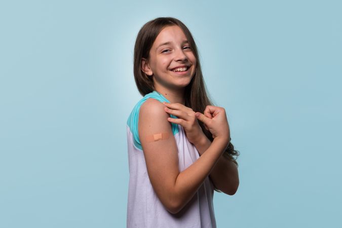 Girl flexing arm with bandage after receiving vaccination.