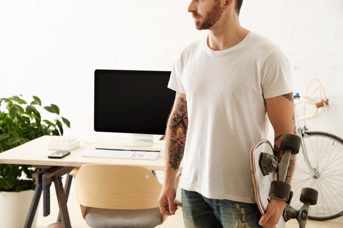 Tattoooed man in blank t-shirt holds surf skateboard