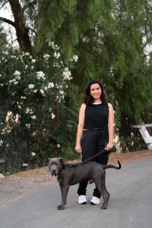 Full length shot of woman in casual athletic attire standing with her dog on the street