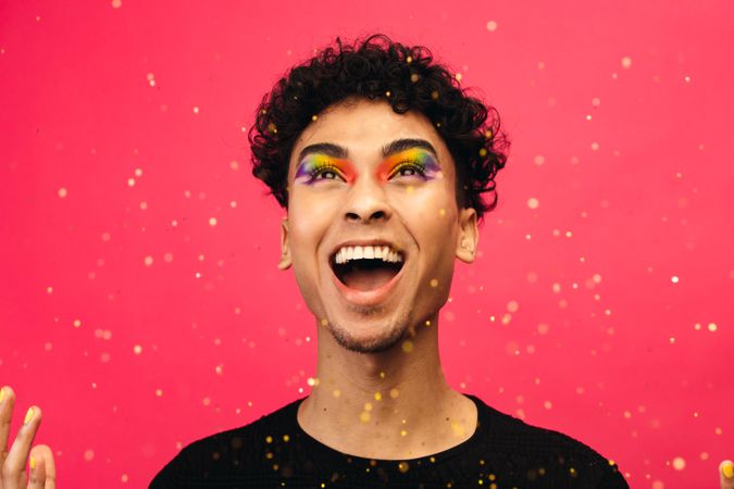 Male with rainbow eye makeup throwing up the glitter and laughing