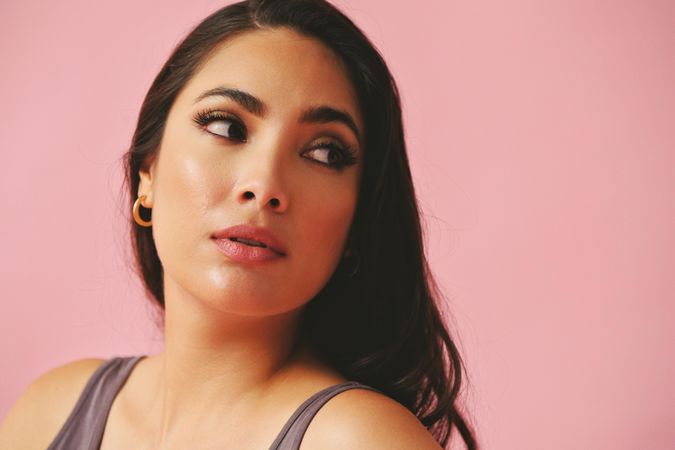 Serious Hispanic woman looking away from camera in pink room