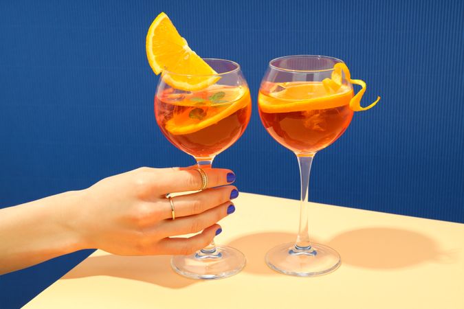 Hand reaching for a summer cocktail garnished with orange slice